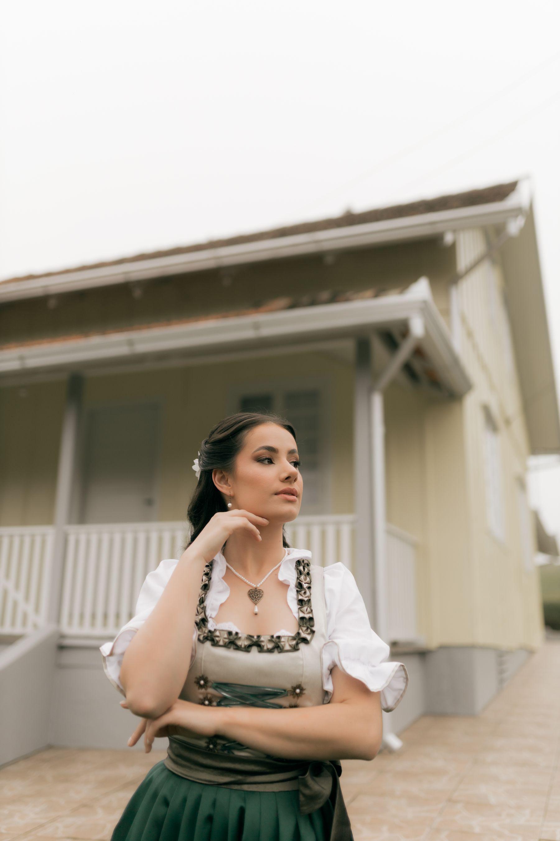 Woman in a traditional green dirndl with a soft braided hairstyle, portrait outside a Bavarian house