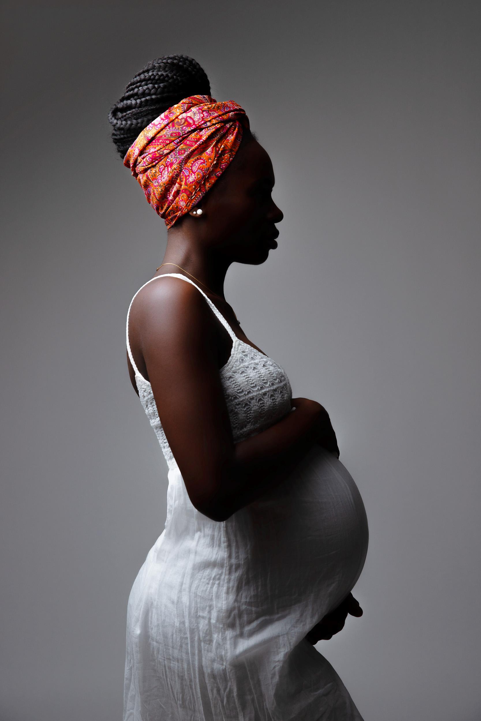 Silhouette maternity portrait wearing a patterned head wrap, profile against a grey backdrop