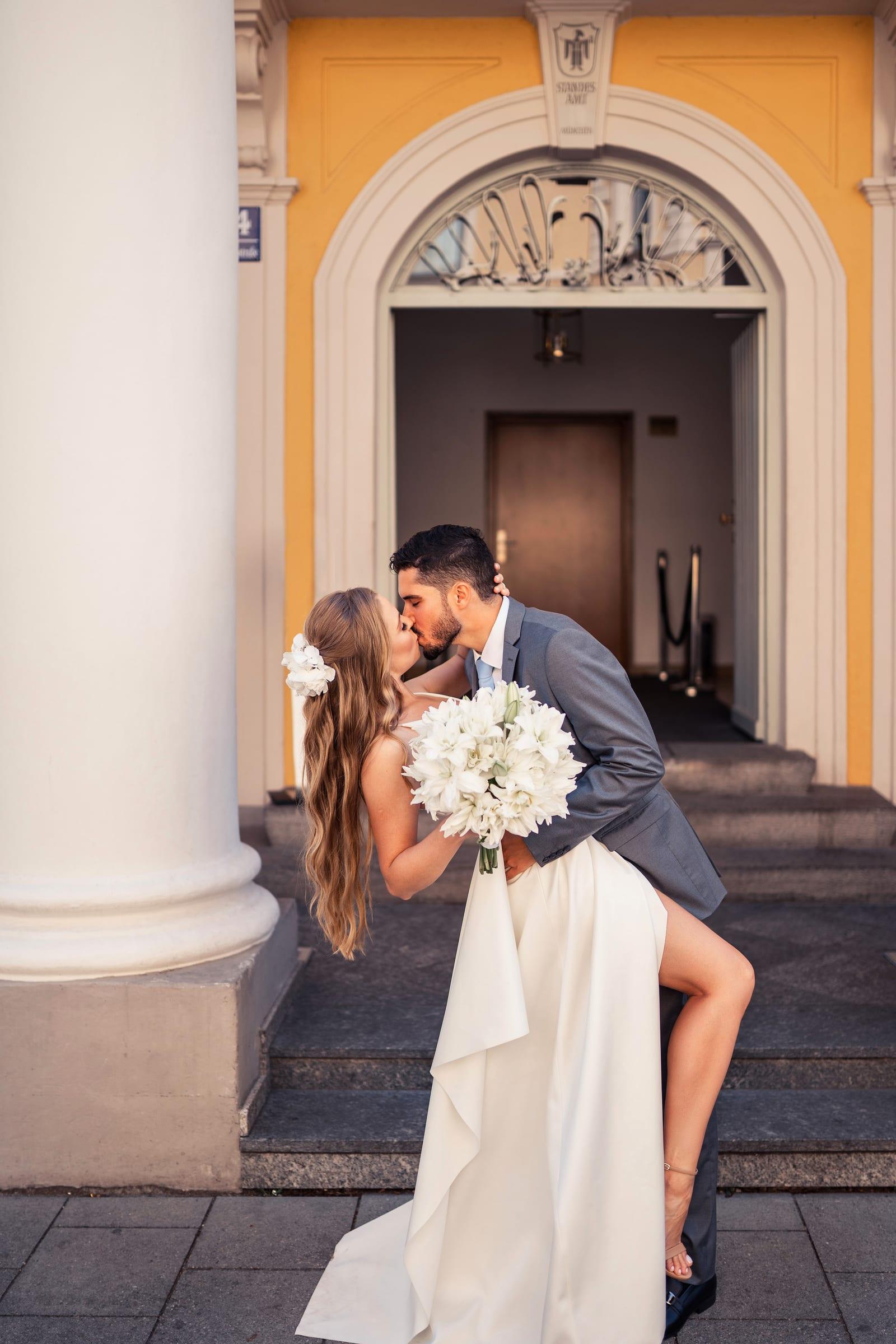 Bride and groom kissing on the steps of a registry office, bride with long loose waves and a white bouquet