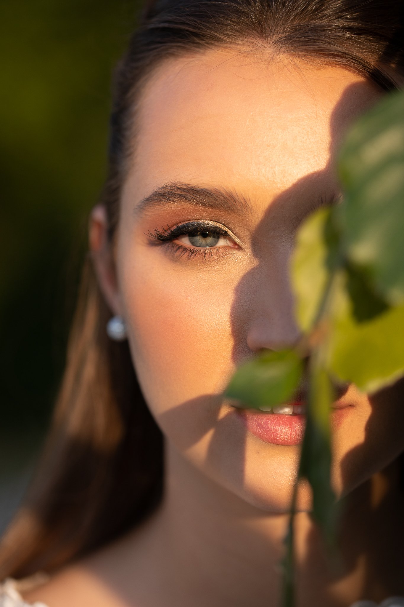 Close-up of a bride's glowing skin and warm bronze eye makeup, face partly framed by leaves