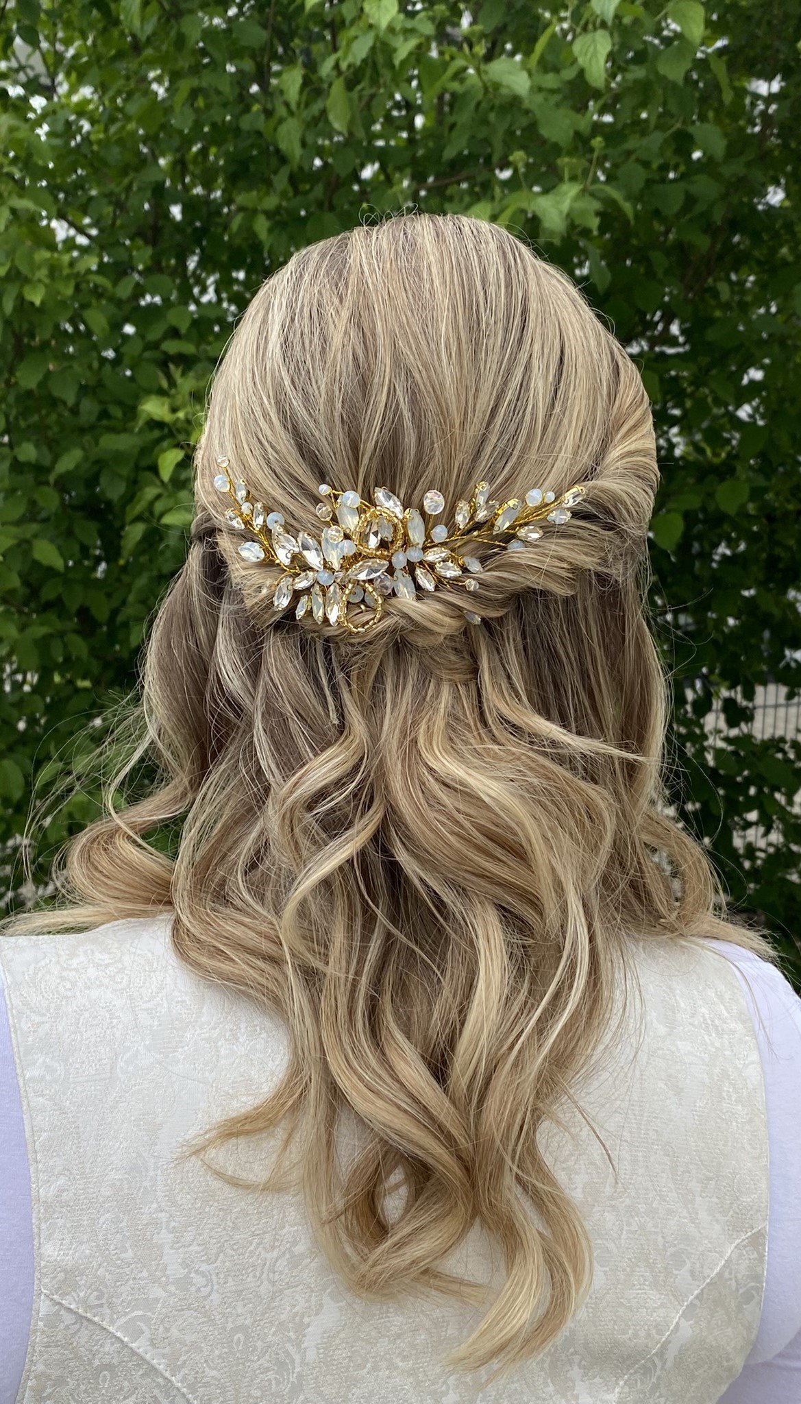 Back view of a half-up bridal hairstyle with soft blonde waves and a gold floral hair comb