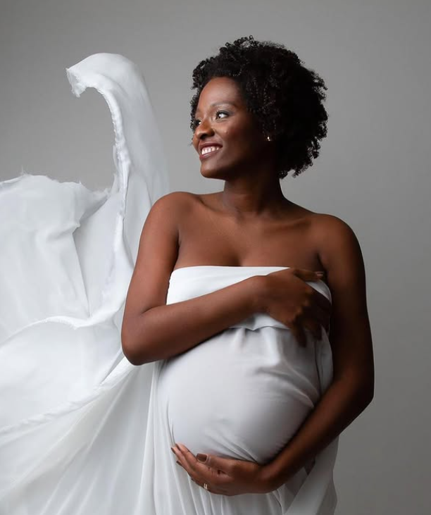 Smiling maternity portrait in draped white fabric against a soft grey backdrop