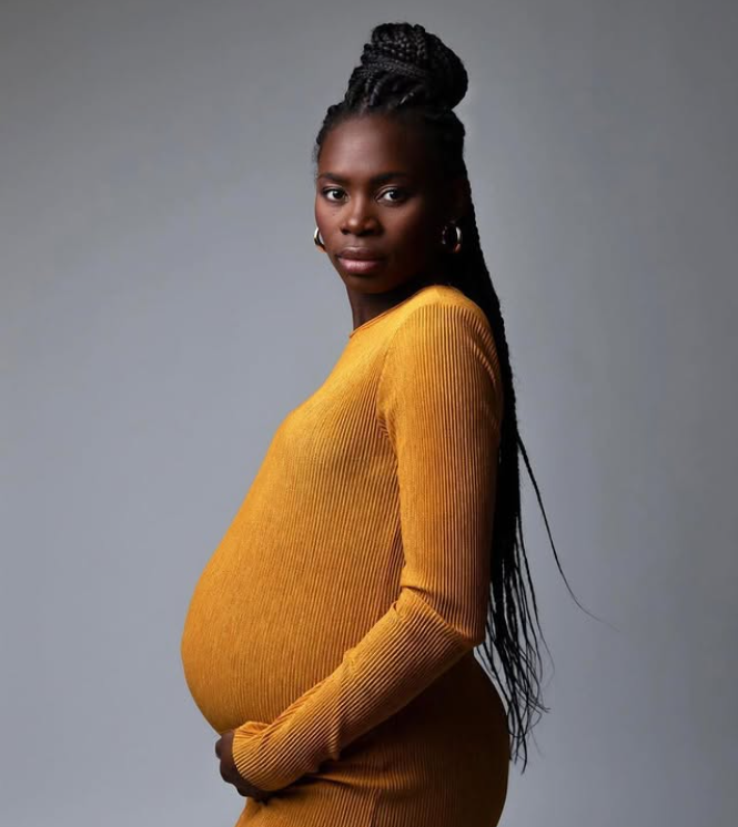 Maternity portrait in a mustard knit dress, hands cradling the belly, profile view